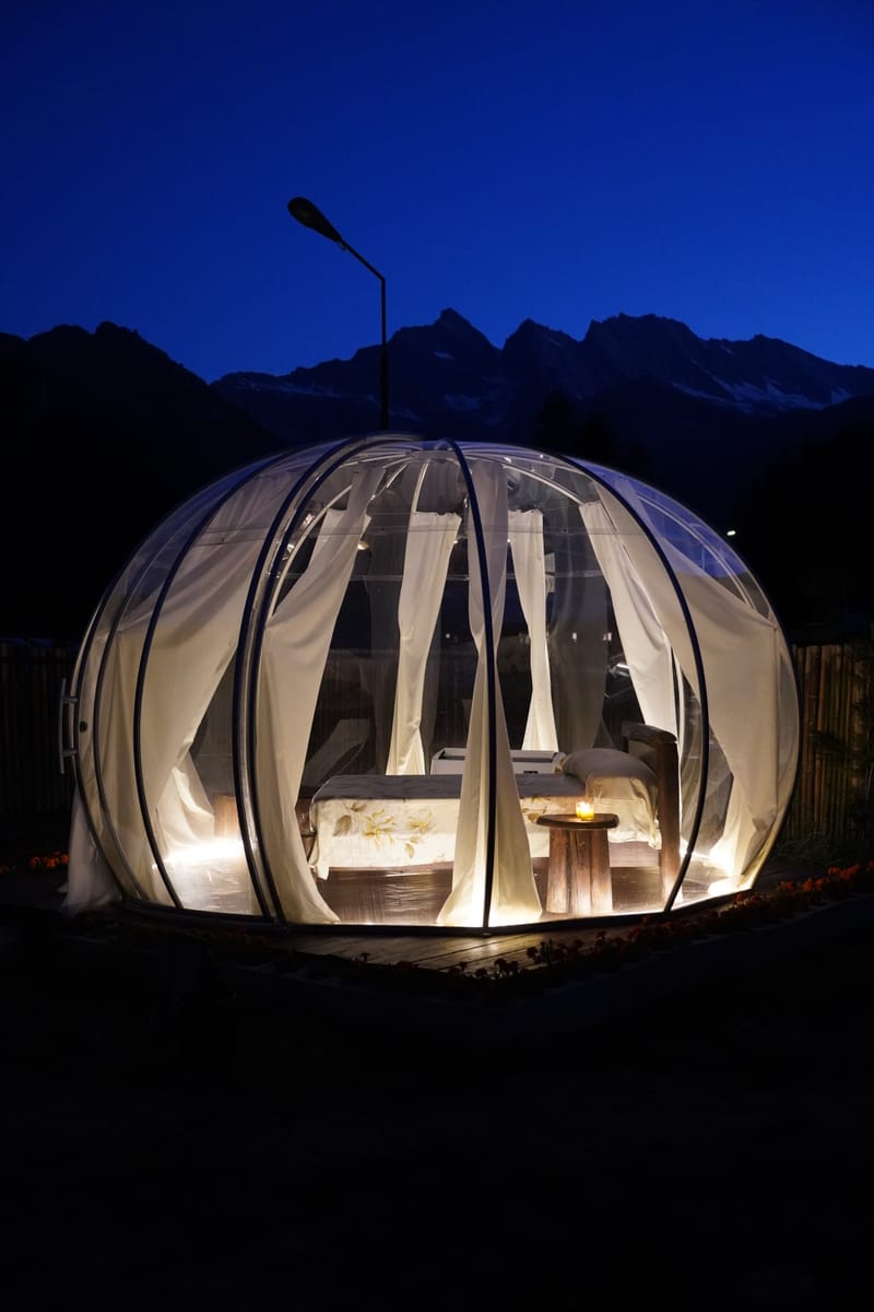 Cupola glamping illuminata di notte davanti alle Alpi